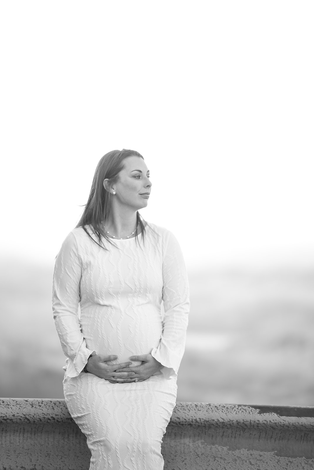 Maternity portrait of woman in field at dusk, mountains visible behind her, soft dramatic evening light