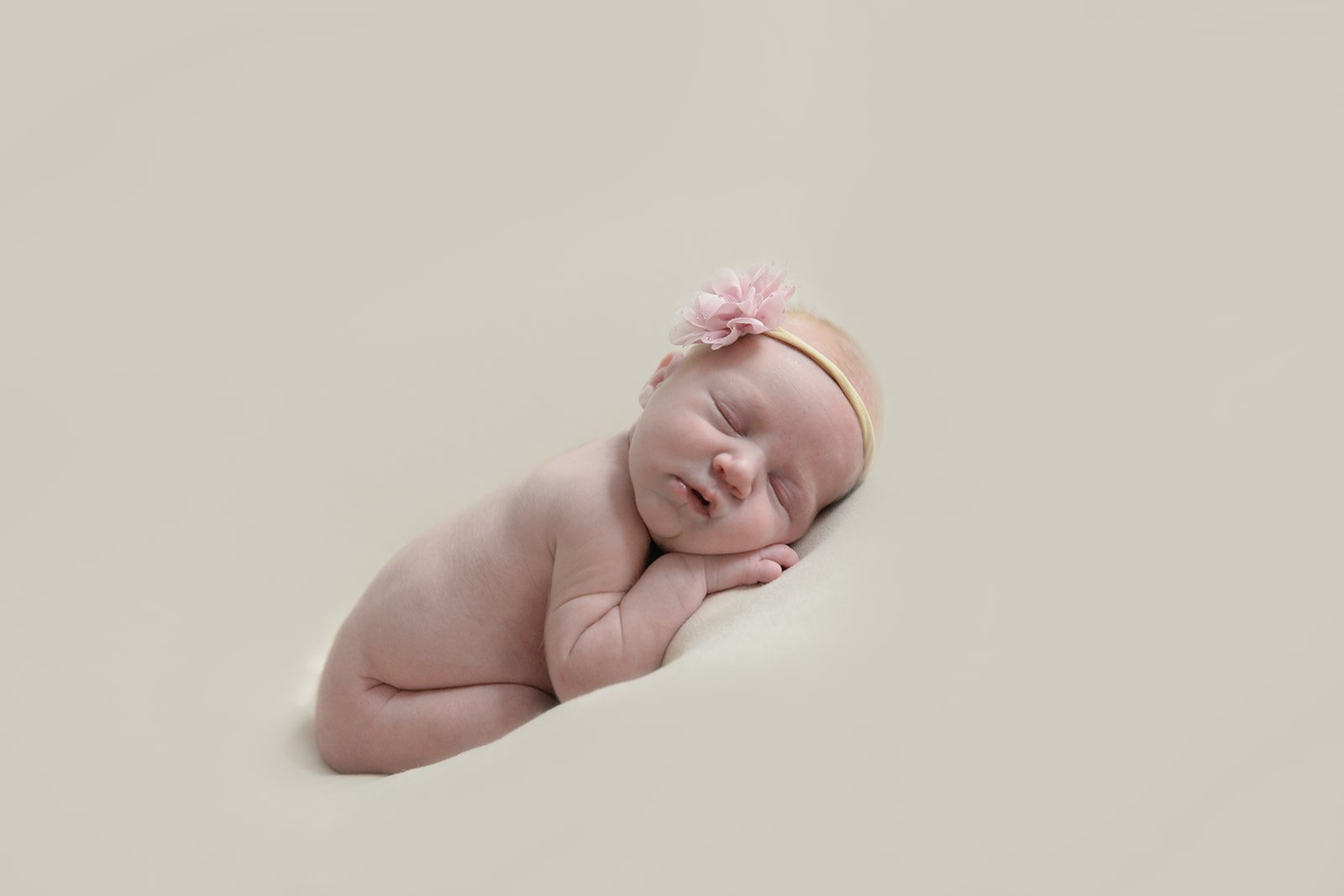 A bare newborn sleeping on a cream blanket with a soft pink flower headband — Northwest Georgia studio newborn session